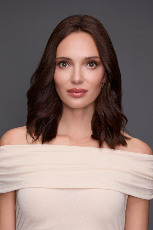 Woman wearing a beige off-shoulder dress against a gray background