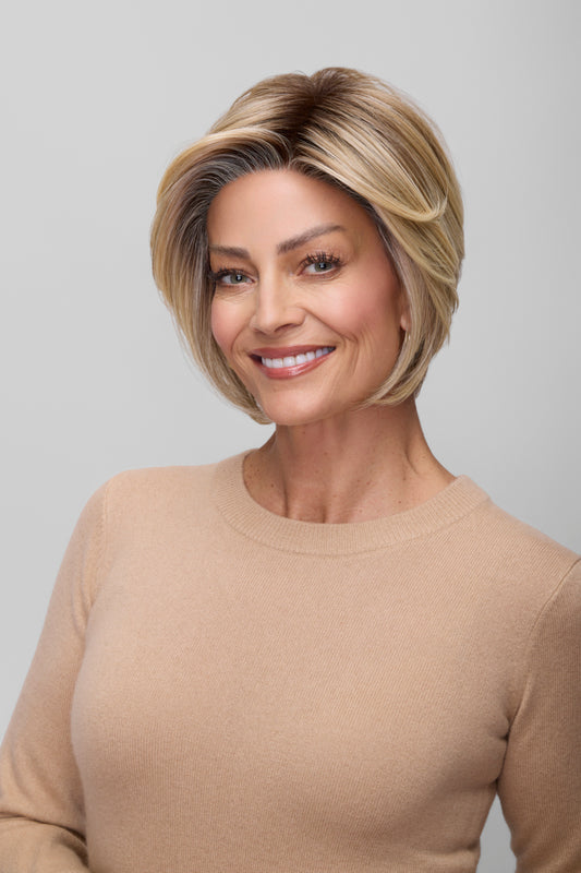 Woman with styled hair wearing a beige sweater against a plain background