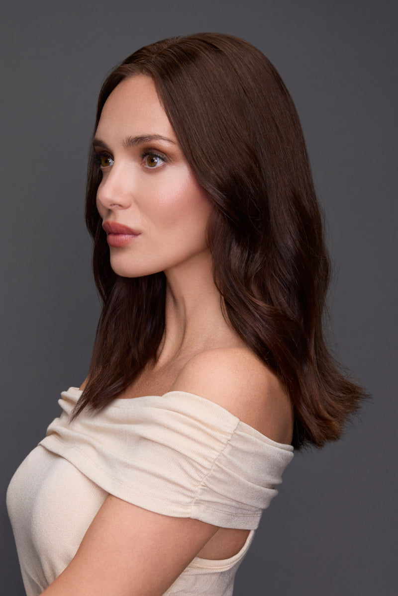 Woman with long brown hair wearing an off-shoulder beige top against a gray background