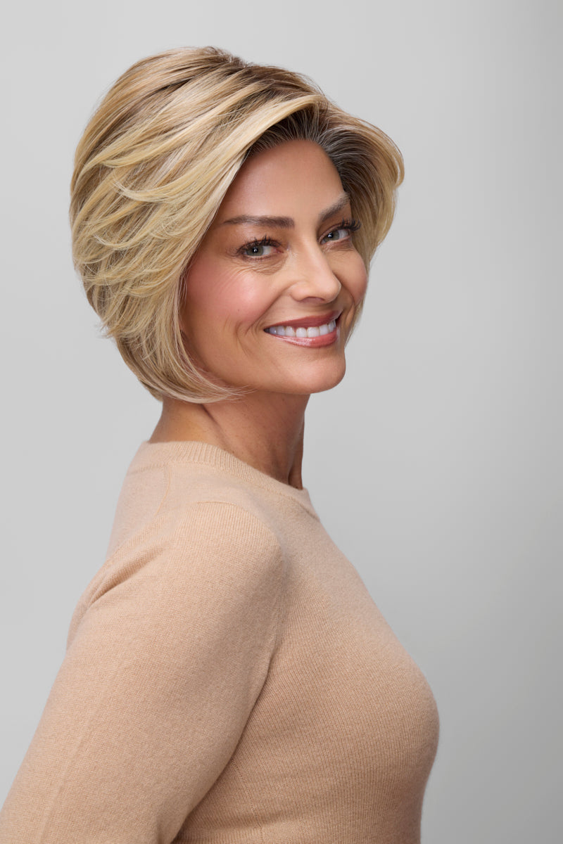 Woman with styled blonde hair wearing a beige sweater on a plain background