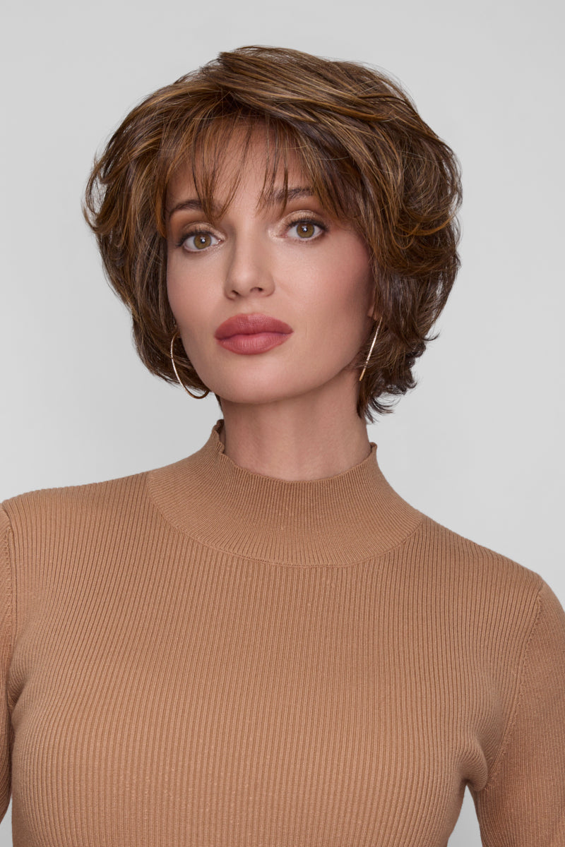 Woman with styled hair wearing a beige sweater against a plain background