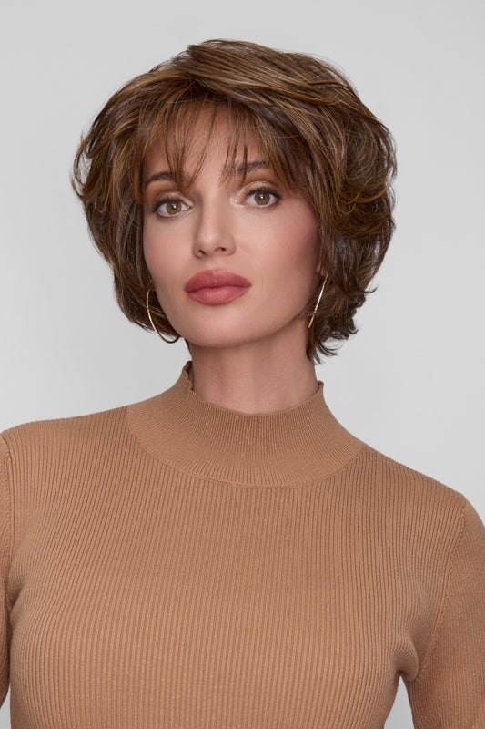 Woman with styled hair wearing a beige sweater against a plain background