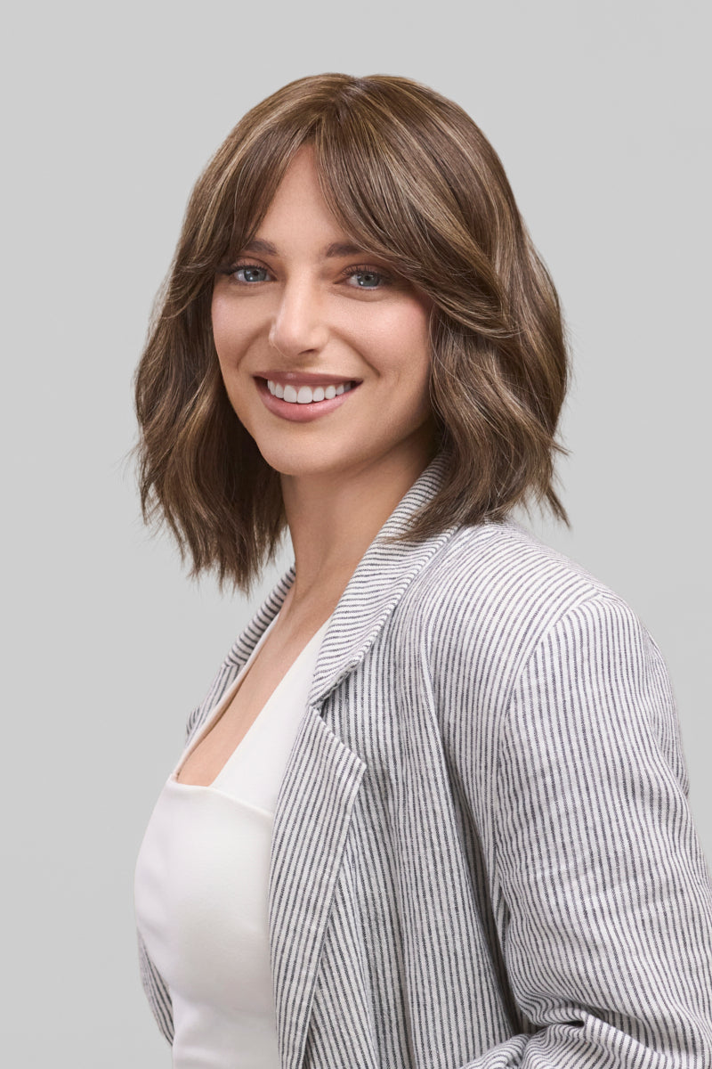 Woman with shoulder-length brown hair wearing a gray blazer over a white top on a light gray background