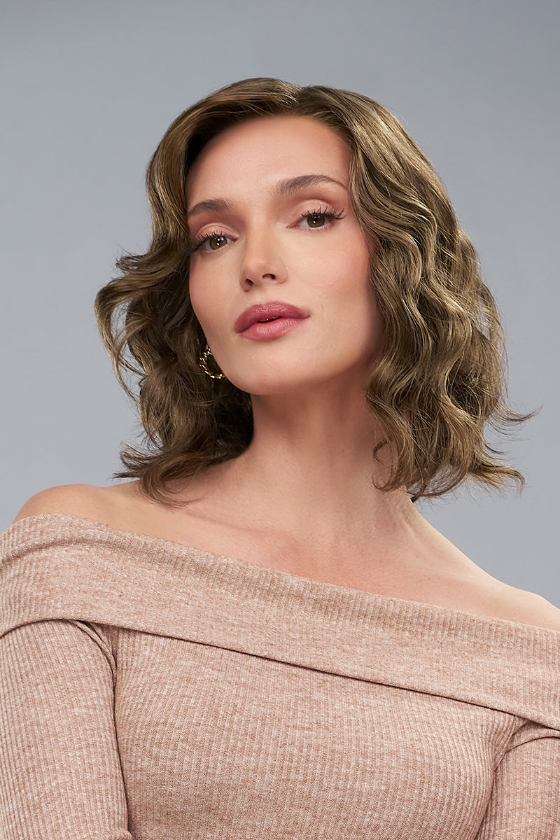 Woman with styled hair wearing an off-shoulder top against a gray background