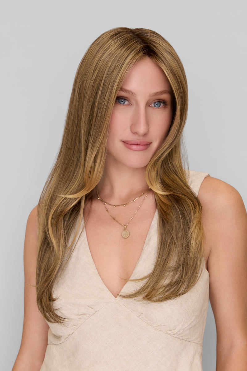 Woman with long blonde hair wearing a beige dress against a plain background