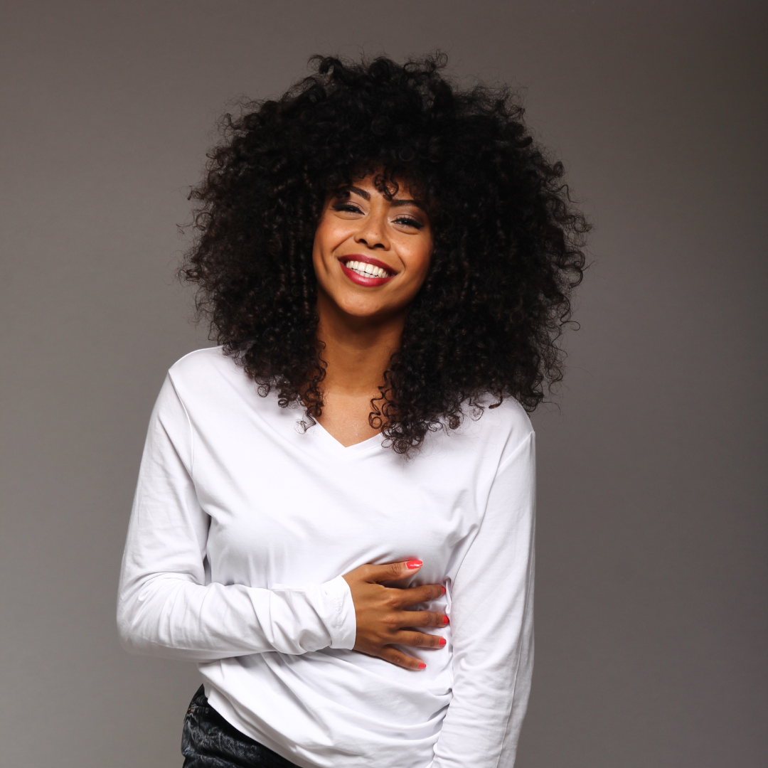 lady smiling with afro kinky hair. Wearing a white top.